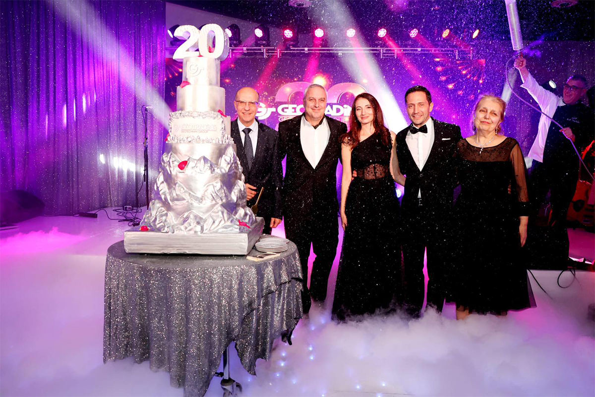 4 people in festive costumes standing behind cake with number 20 and celebrating